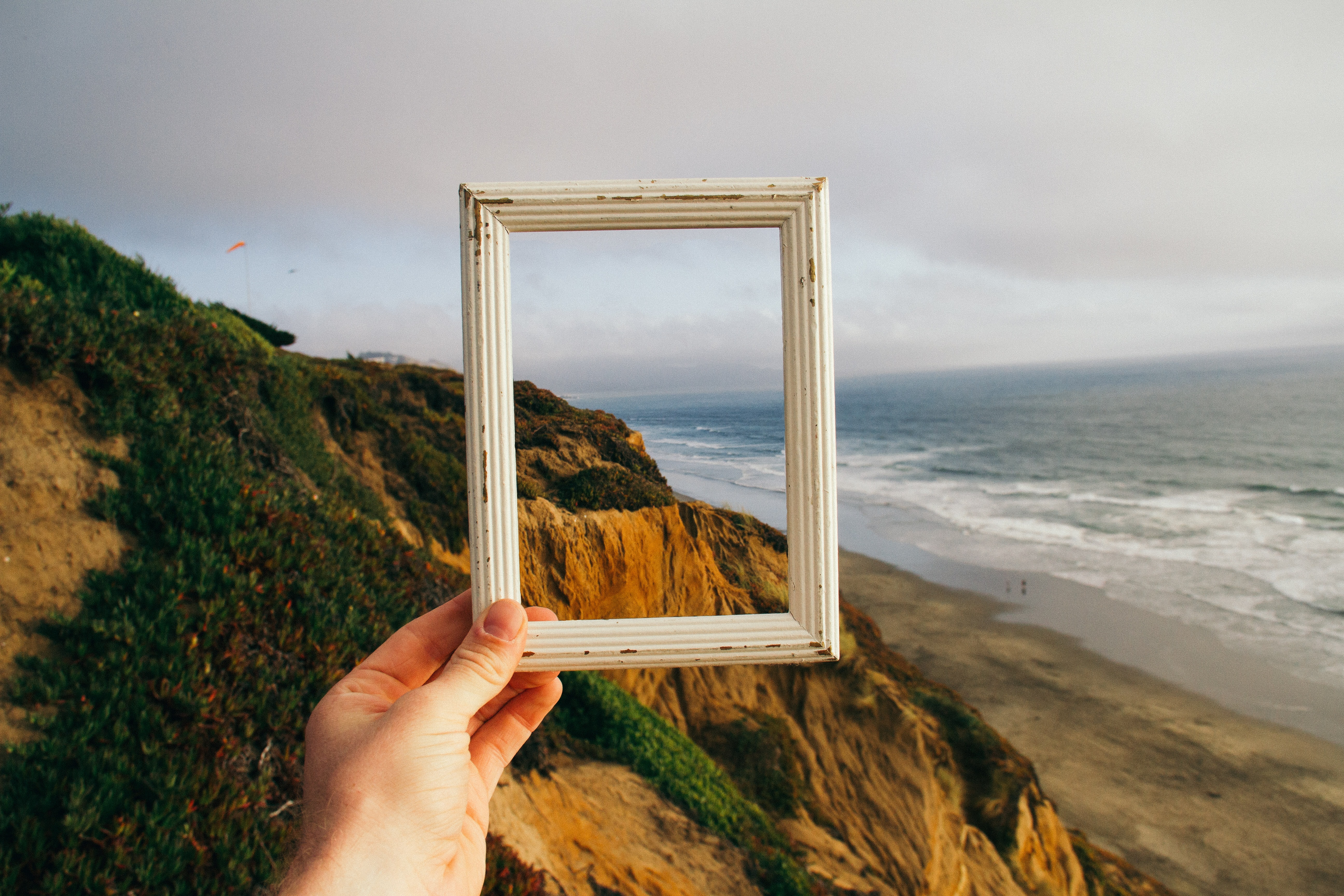 A hand holding an empty frame in front of a cliff by the sea